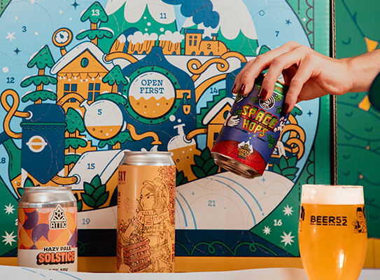 hand reaching into the advent calendar box surrounded by craft beer cans and a full glass